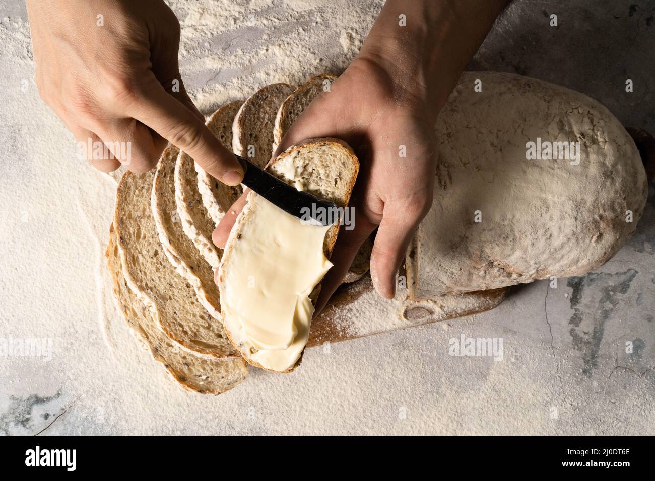 Uomo spalmando burro di formaggio cremoso o una fetta di pane su tavola di legno. Pane da dieta. Primo piano. Concetto di nutrizione sana. Foto Stock