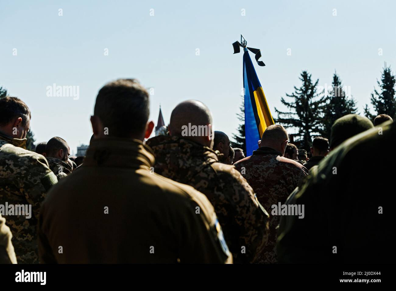 UZHHOROD, UCRAINA - 18 MARZO 2022 - le file di soldati fronteggiano una bandiera Ucraina legata con un nastro nero durante i funerali militari di tre ucraini Foto Stock