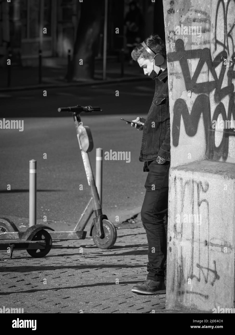 Bucarest, Romania - 02.04.2022: Giovane uomo che indossa le cuffie che naviga o SMS sul suo smartphone sul marciapiede, a Bucarest. Fotografia di strada. Foto Stock