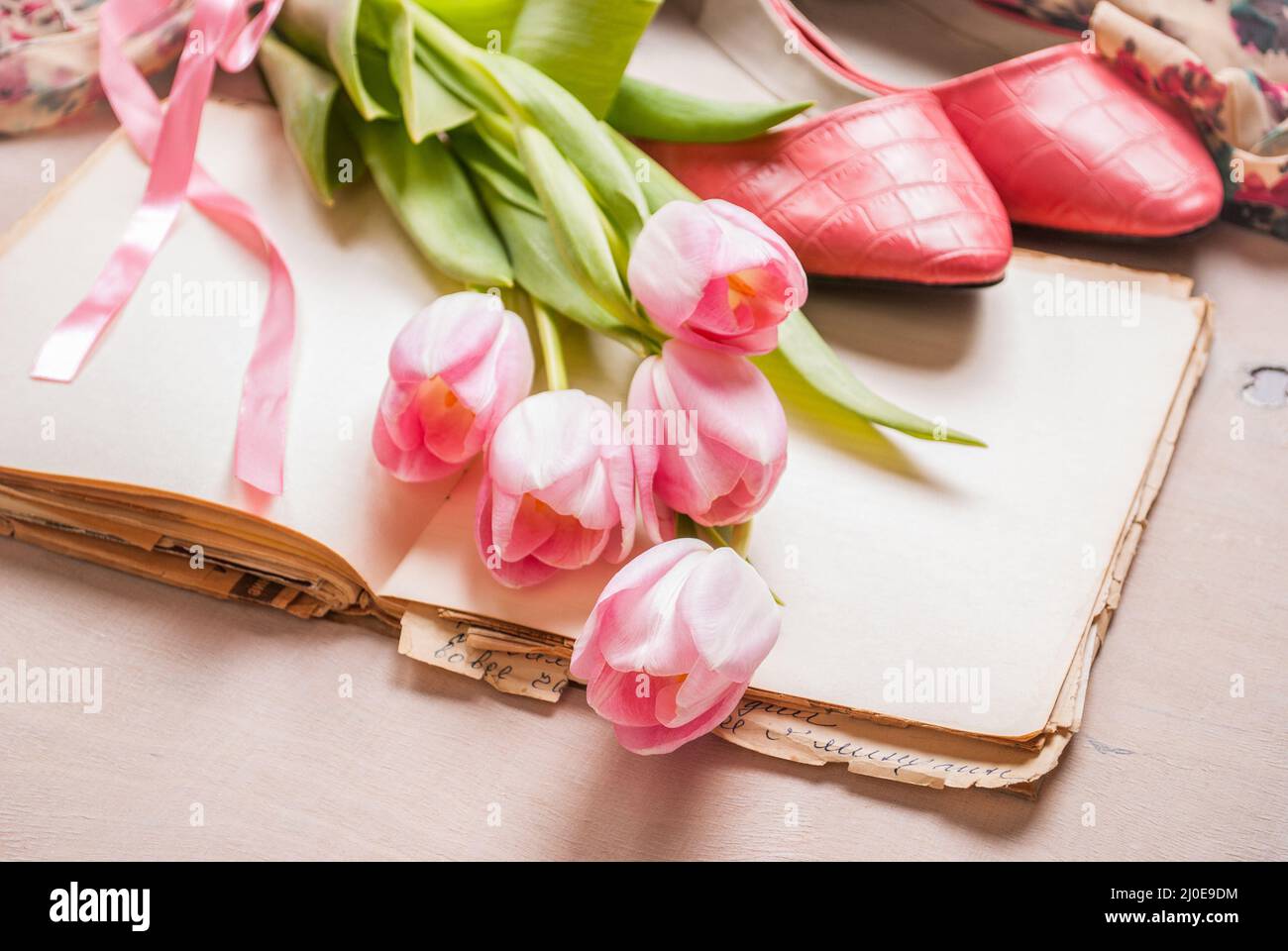 Tulipani rosa e libro bianco con scarpe donna su bianco tavolo in legno. Molla di sfondo chic Foto Stock