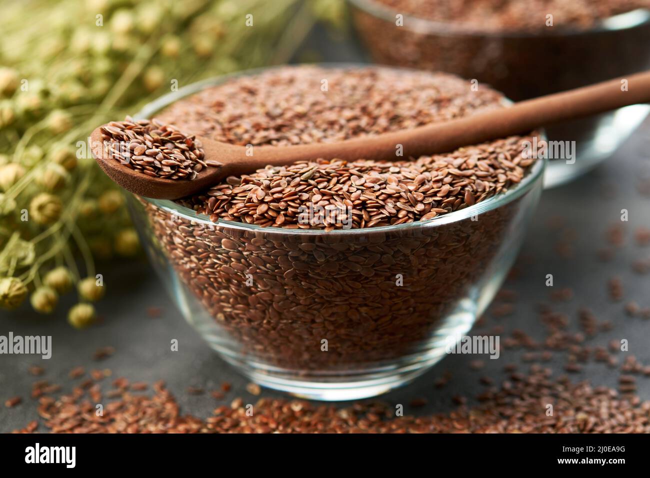 Ciotola di semi interi di lino. Tazza di vetro di semi di lino, mazzo di piante di lino su tavola. Foto Stock