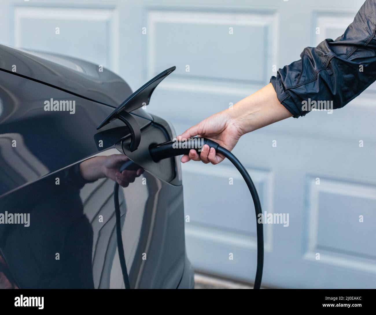 I caricabatterie si collegano all'auto elettrica. Mani femminili inserimento di un caricabatteria nella presa per auto elettrica Foto Stock