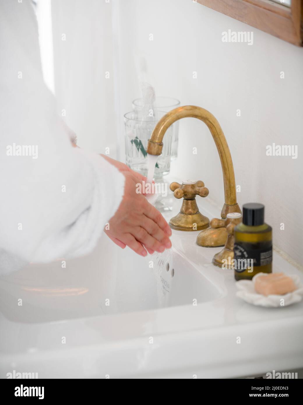 Foto verticale di un classico lavandino del bagno con una donna che lava le mani in un accappatoio Foto Stock