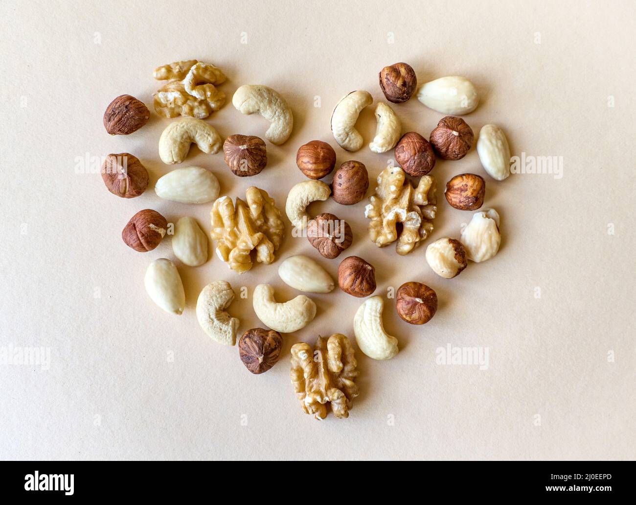 Una varietà di noci, noci, mandorle, nocciole e anacardi disposti in modo da l'aspetto come la forma di un cuore isolato su sfondo beige Foto Stock