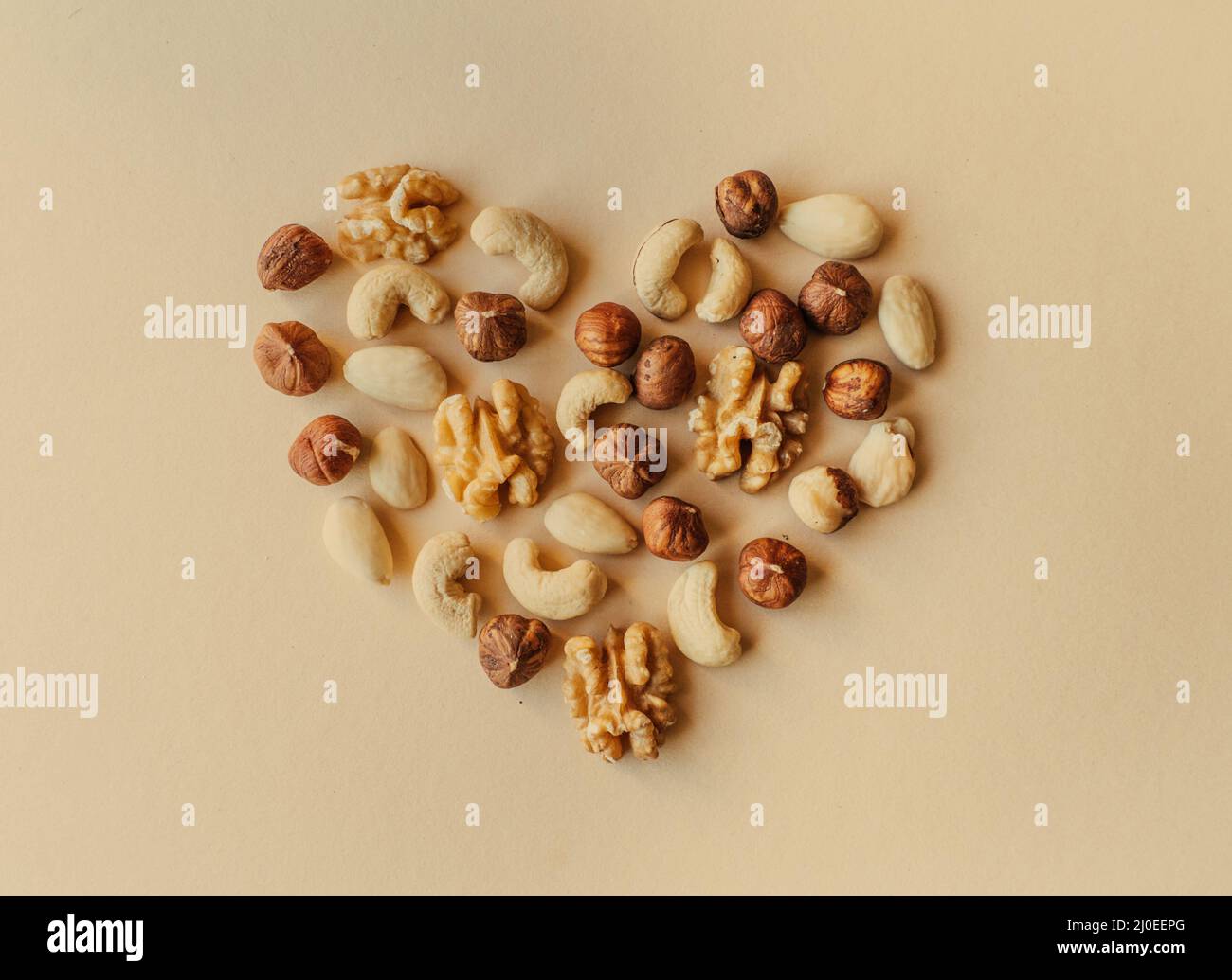 Una varietà di noci, noci, mandorle, nocciole e anacardi disposti in modo da l'aspetto come la forma di un cuore isolato su sfondo beige Foto Stock