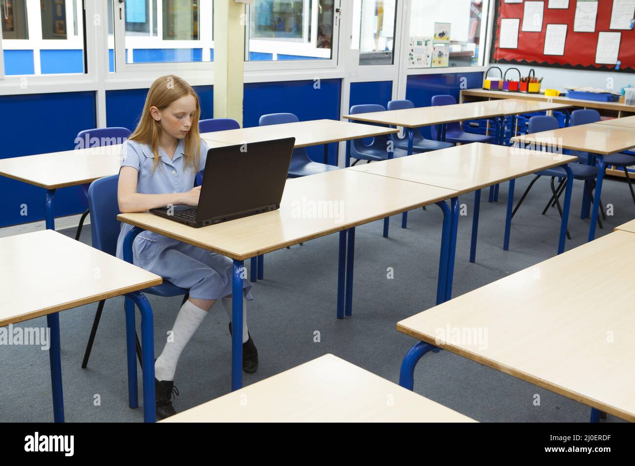 Scuola primaria ragazza caucasica usando un computer portatile in un aula vuota Foto Stock