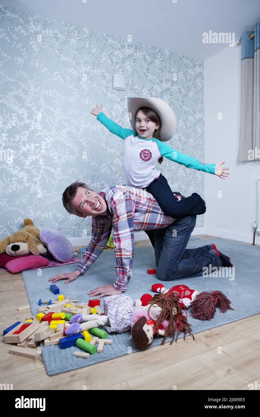 Pre-teen ragazza caucasica avente un piggyback ride da suo padre nella loro lounge Foto Stock