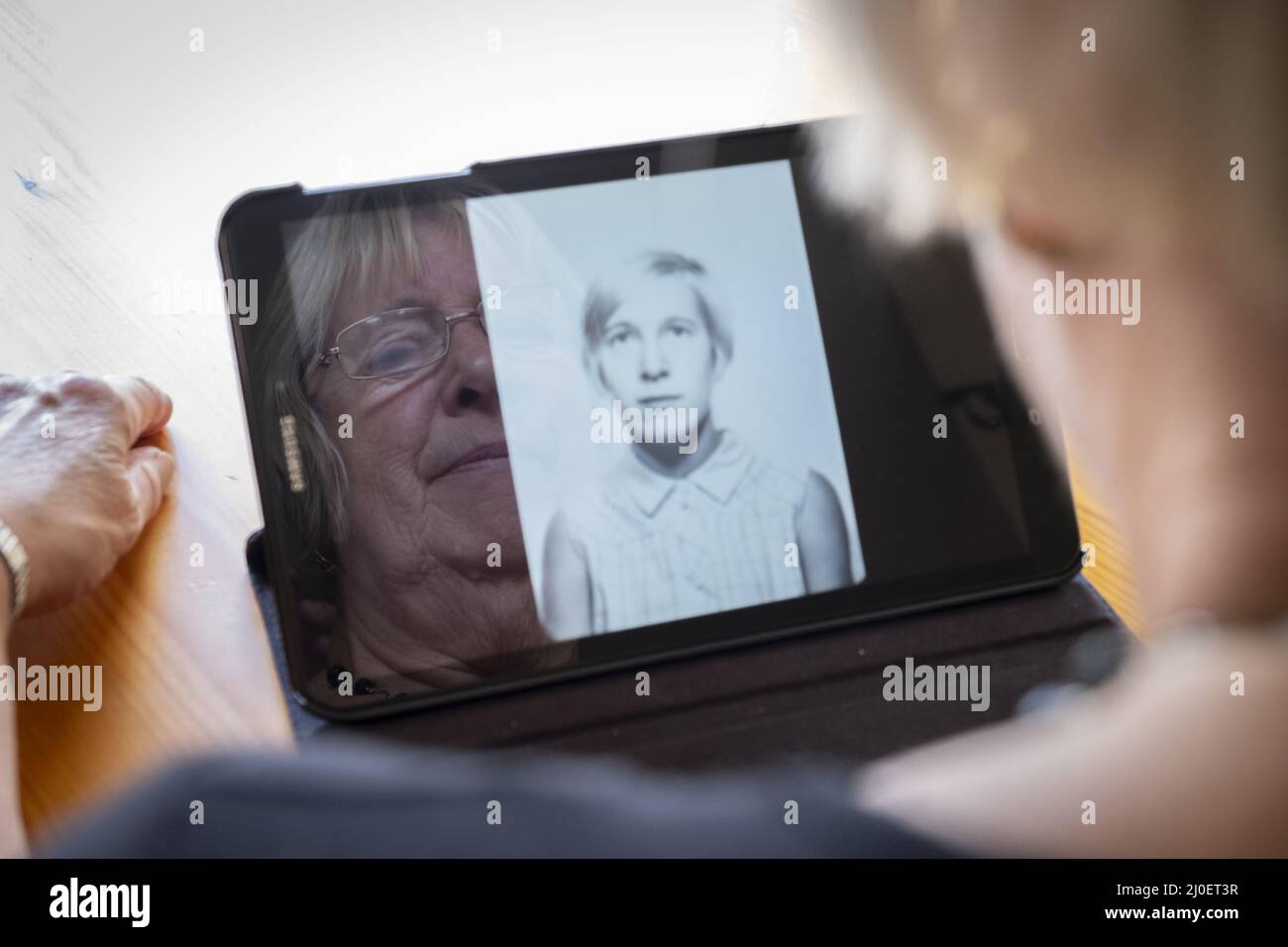 Senior donna caucasica guardando le vecchie foto di se stessa come una giovane donna in un computer tablet Foto Stock