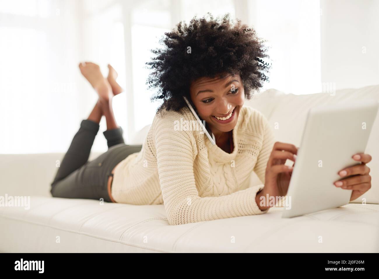 Im appena circa per leggere il vostro blog. Scatto di una giovane attraente utilizzando il suo cellulare e tablet mentre si trova sul divano a casa. Foto Stock