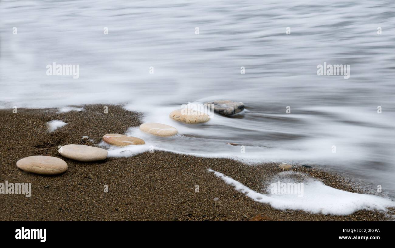 Pietre di spiaggia in una fila e onde di mare Foto Stock