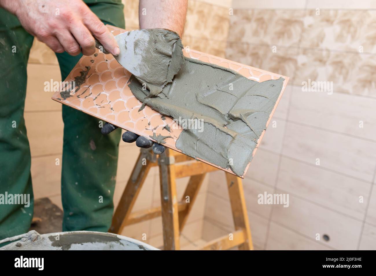 Un operaio di costruzione applica l'adesivo di cemento ad una piastrella di ceramica e lo sparge completamente sopra l'intera superficie. Foto Stock