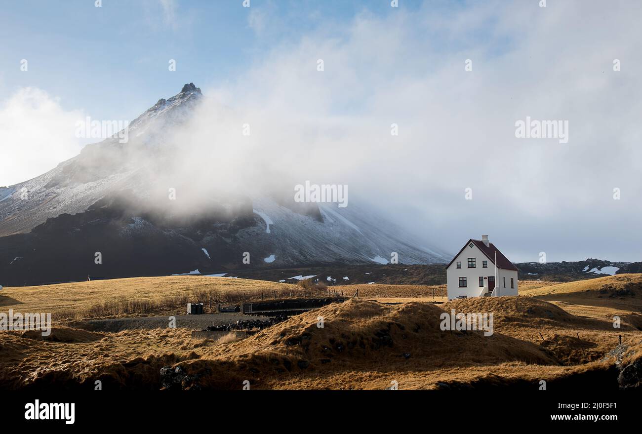 Casa solitaria nel piccolo villaggio di pescatori di Arnarstapi e scogliera di montagna coperta di neve a SnÃ¦f Foto Stock