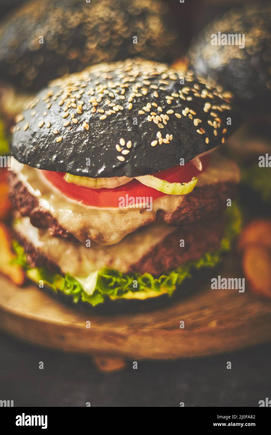 Hamburger doppi neri con formaggio. Cheeseburgers dal Giappone con panino nero su sfondo scuro Foto Stock