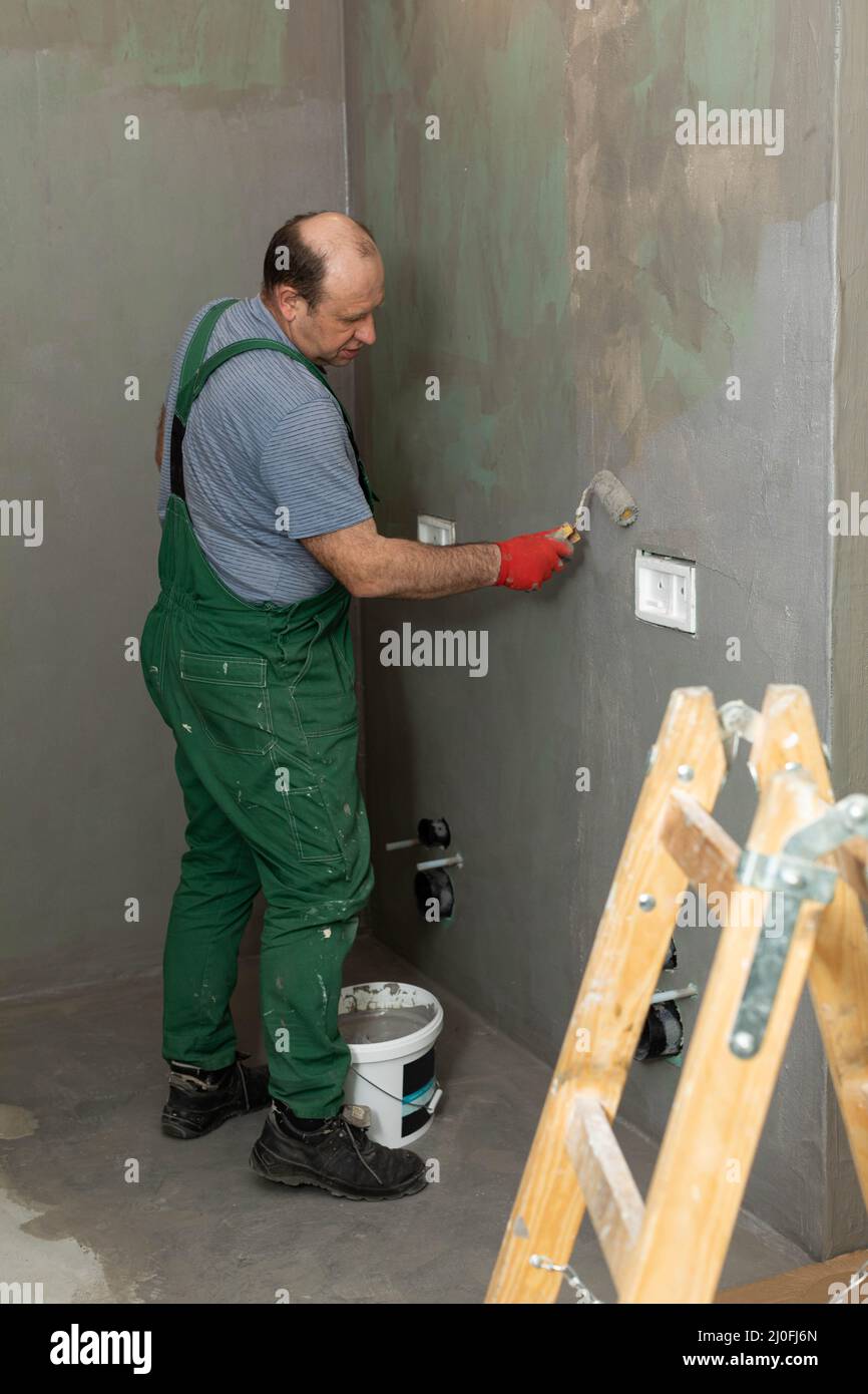 Un operatore di costruzioni esperto applica un isolamento umido con un rullo di vernice alla parete. Foto Stock