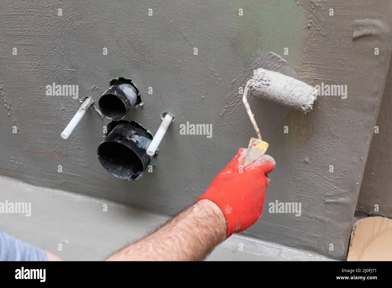 Una vista ravvicinata di un operatore edile esperto che applica un isolamento umido utilizzando un rullo di vernice su una parete. Foto Stock