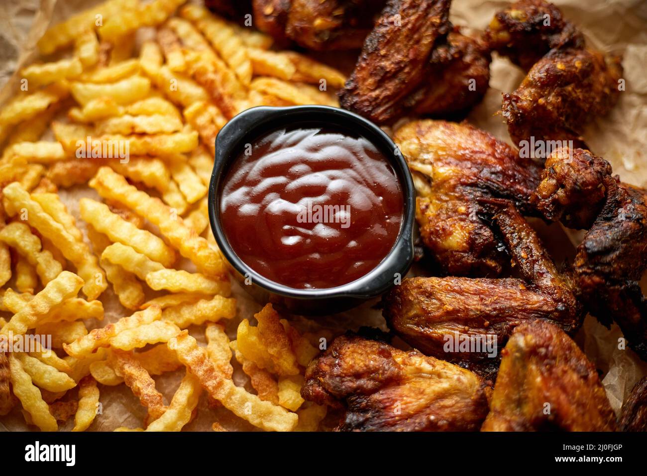 Appetitose ali di pollo arrosto e patatine fritte con salsa al barbecue, servite su carta da forno Foto Stock