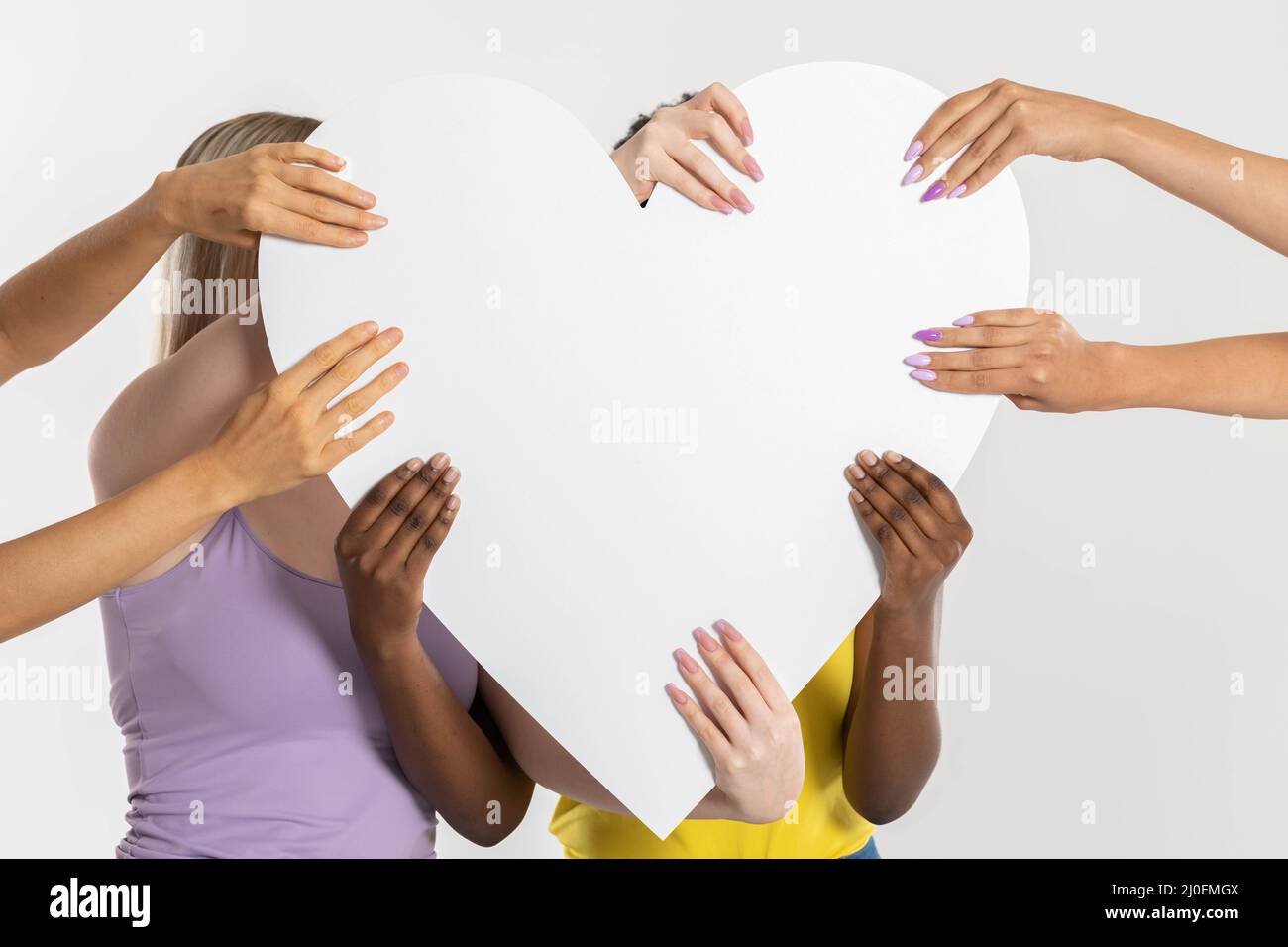 Un grande cuore bianco tenuto da otto mani colorate di nazioni e razze diverse. Molte razze ma un cuore puro comune. Foto Stock