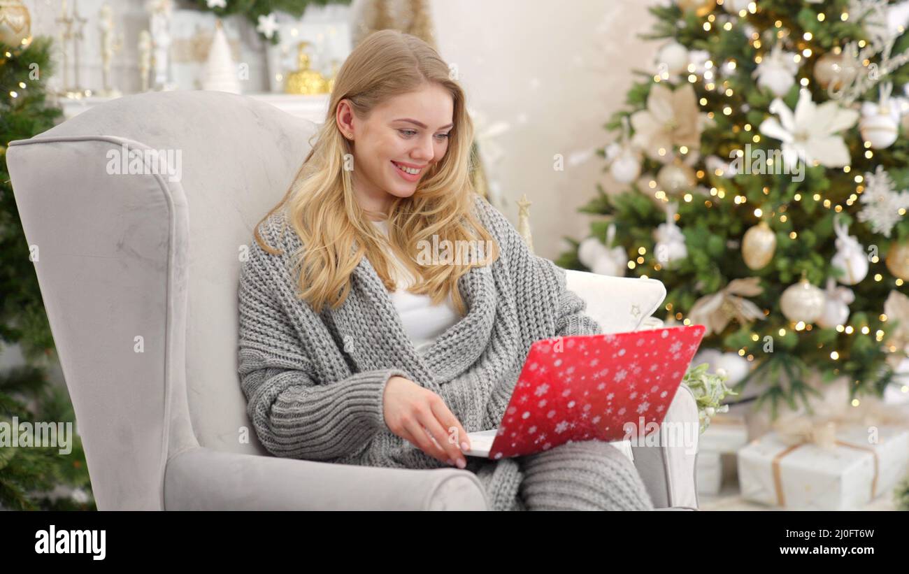 Ritratto di donna sorridente che tiene il laptop sui giri e lavora. Seduta su una comoda poltrona Foto Stock