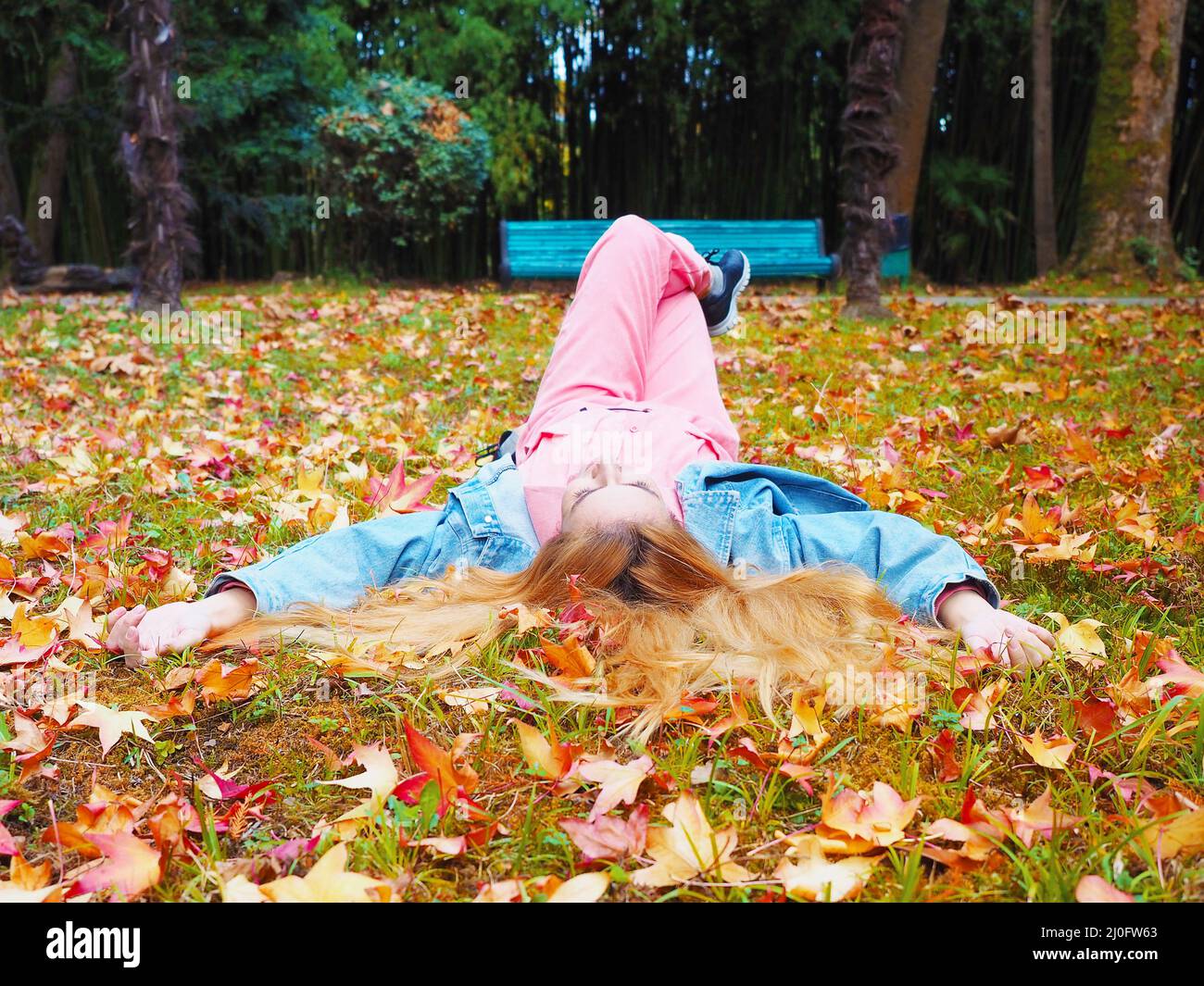 Bambina rossa si trova con le gambe incrociate in un parco su un prato cosparso di foglie d'autunno Foto Stock