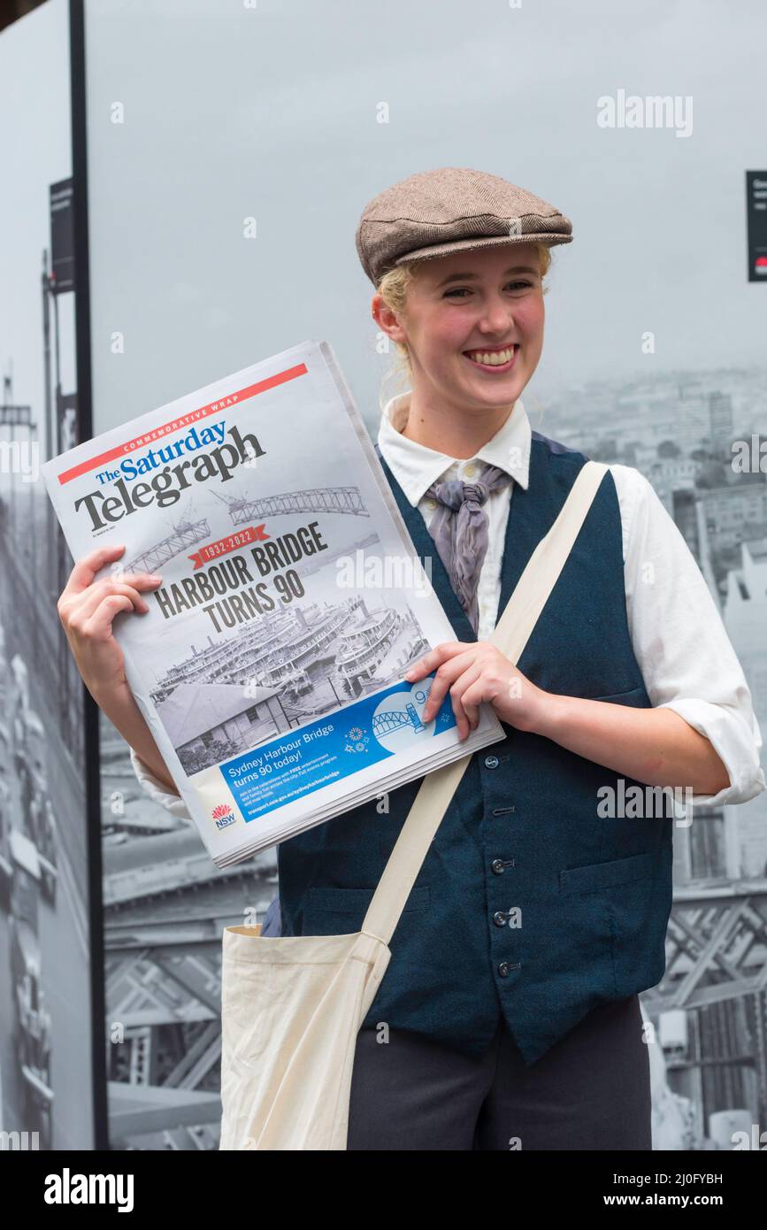 19th marzo 2022, Sydney Australia: Una donna vestita come un ragazzo di carta degli anni '30, consegna gratuitamente Sabato Telegraph giornali (Murdoch Press) il giorno del 90th compleanno celebrazione dell'apertura del Sydney Harbour Bridge. Il ponte ha impiegato 8 anni per la sua costruzione ed è stato aperto nel 1932. È conosciuto localmente come il Coathanger. Foto Stock