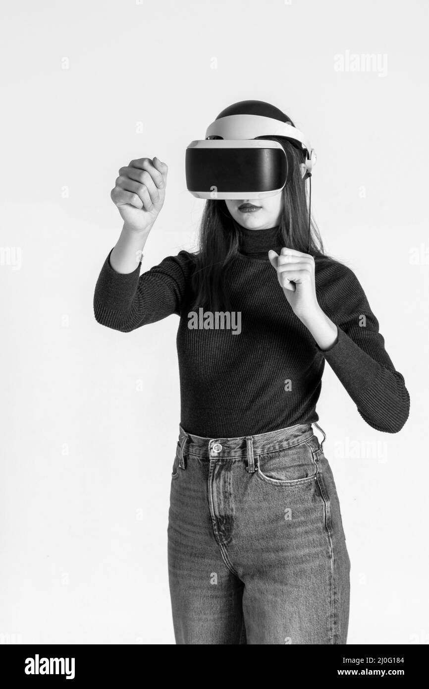 Ragazza adolescente che usa pugni con visore vr, combatte con qualcuno nello spazio di gioco, realtà virtuale su sfondo bianco, cornice verticale, bianco e nero. Virtua Foto Stock