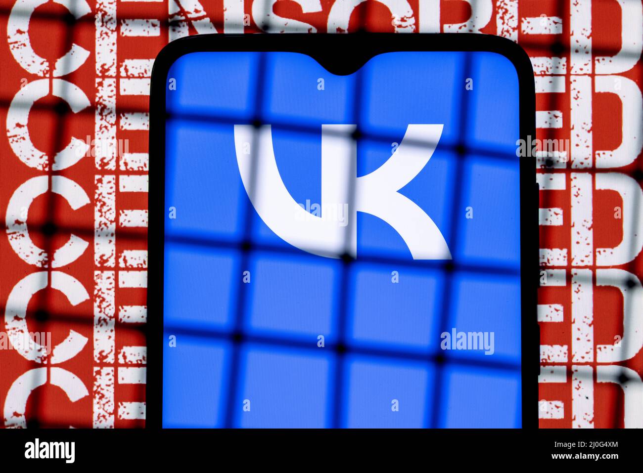 Logo Vkontakte social network sullo schermo dello smartphone dietro le barre sullo sfondo con l'iscrizione censurata. Foto Stock