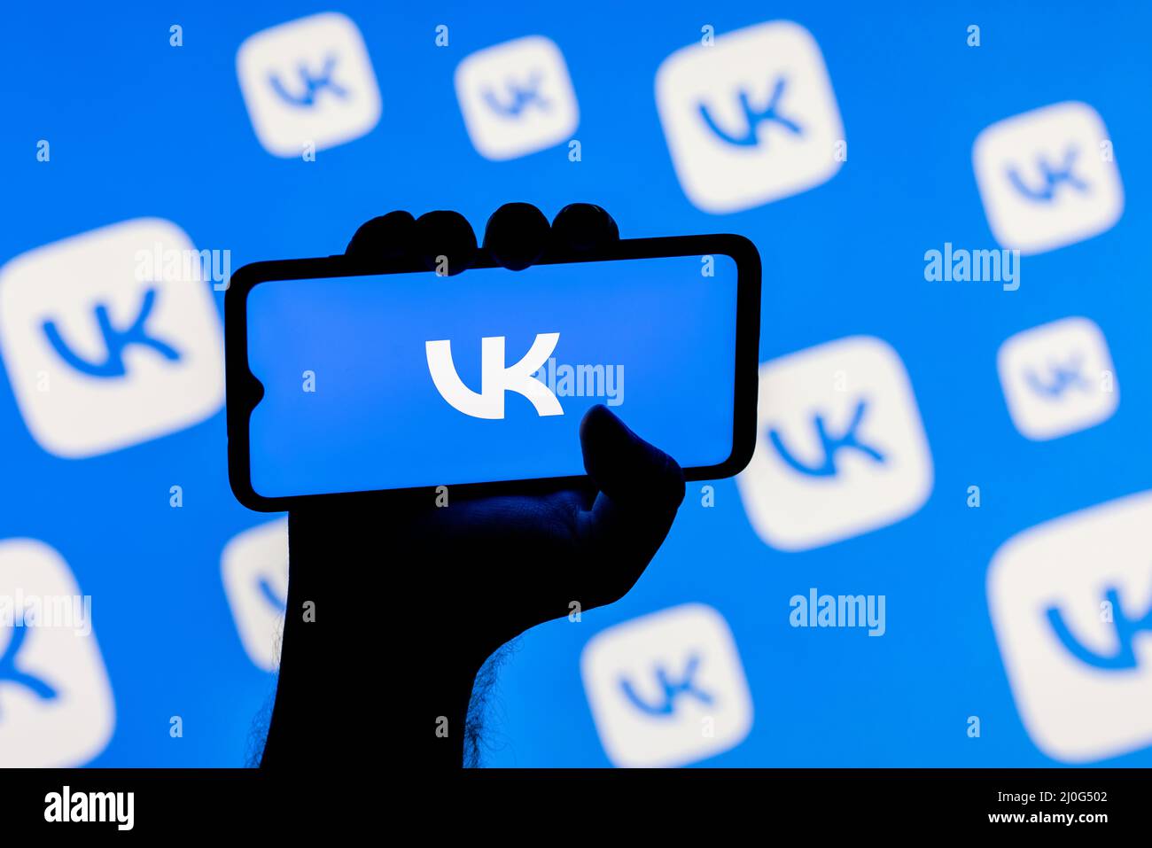 Smartphone con il logo del social network VKontakte sullo schermo in una mano applaiata sullo sfondo dei logo VKontakte Foto Stock