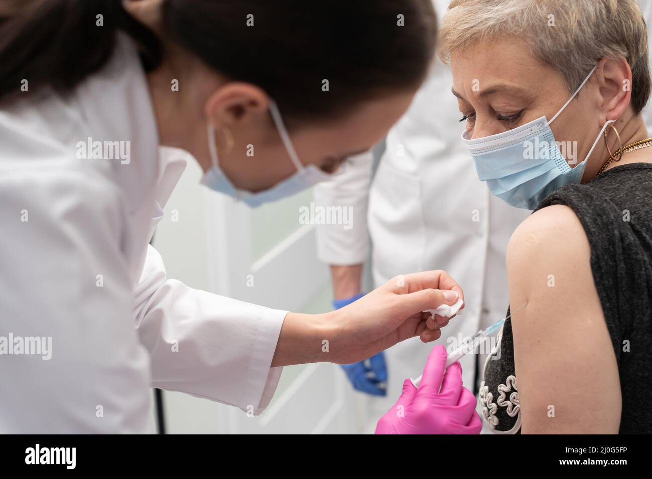 Un infermiere sta facendo un vaccino ad una donna anziana. Il COVID vaccine19. Un ufficio medico sterile in una clinica privata. Un giovane me Foto Stock