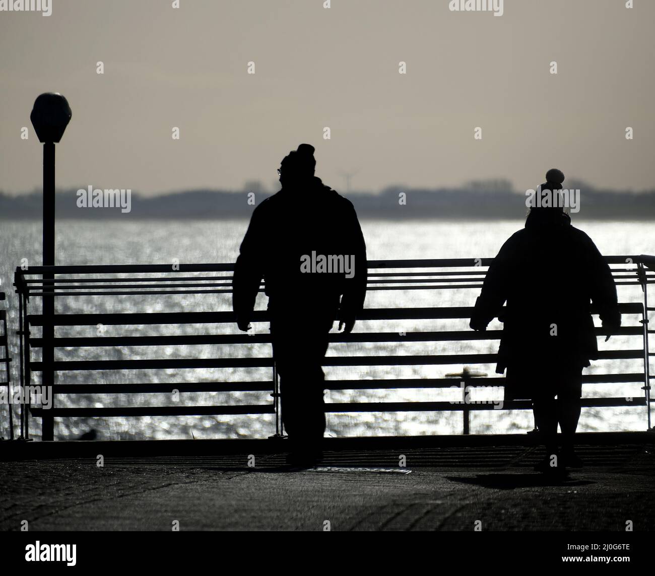Persone in silhoutte guardando oltre recinzione al mare. Foto Stock
