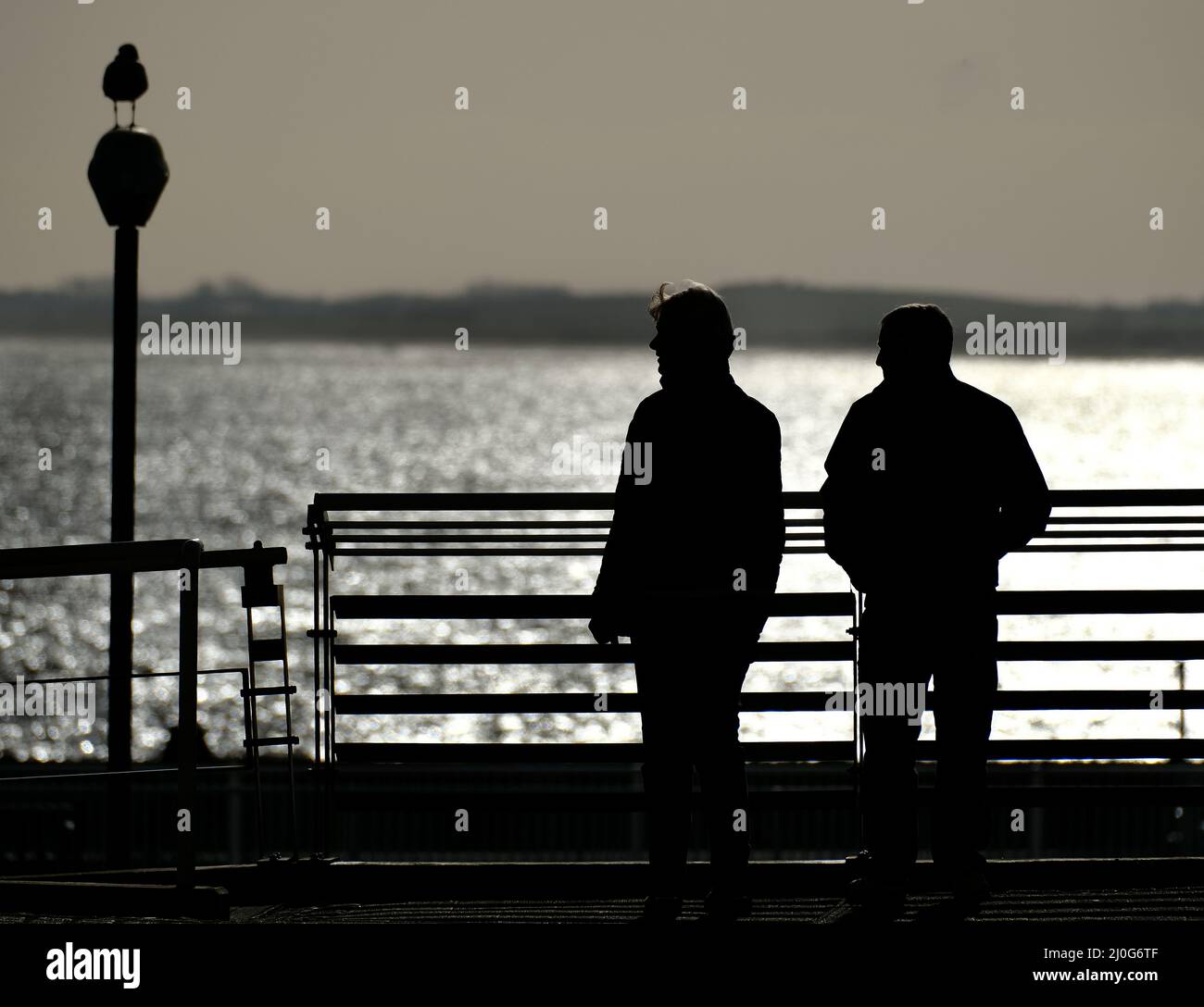 Persone in silhoutte guardando oltre recinzione al mare. Foto Stock