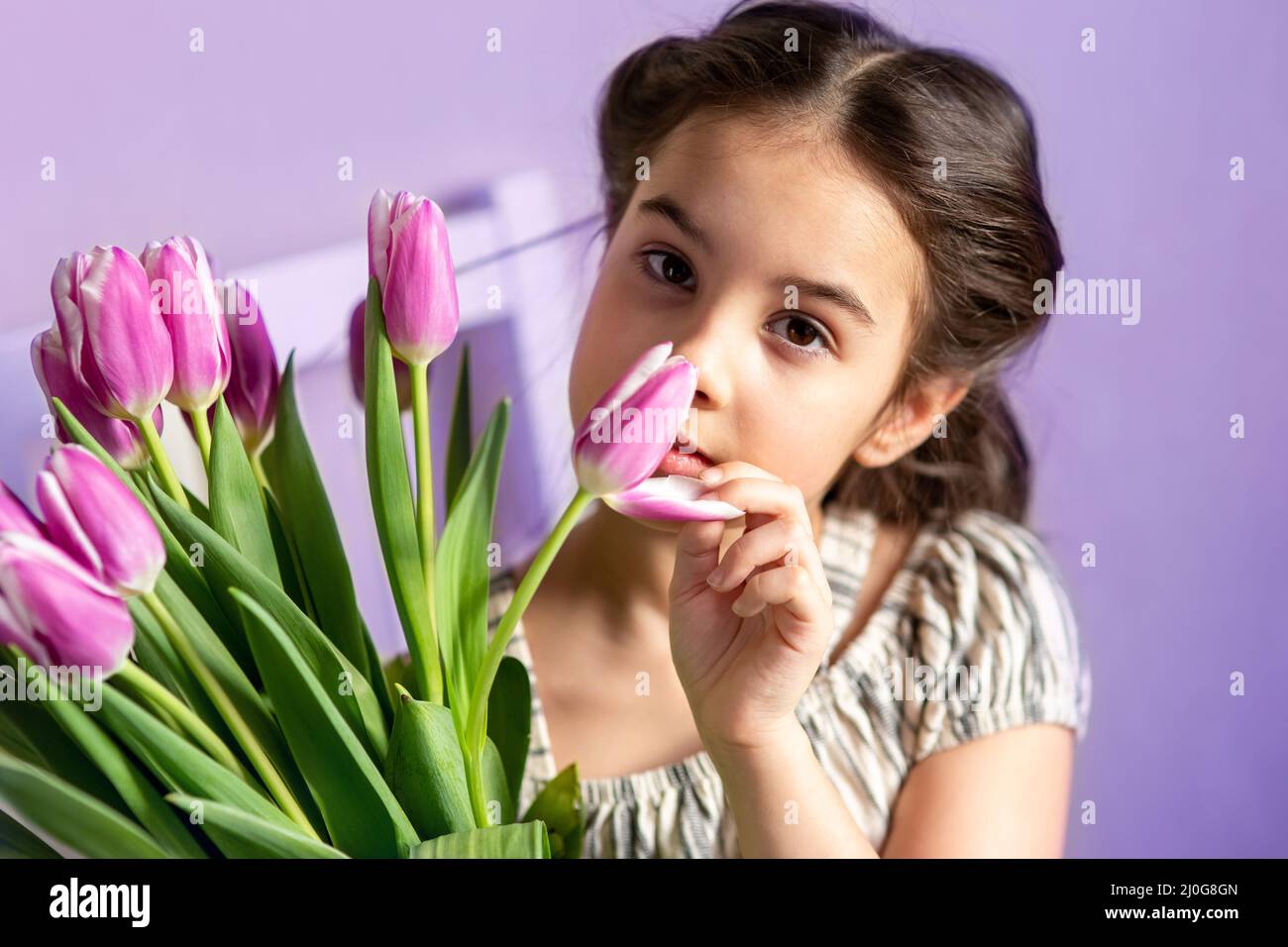 Ritratto di una bella bambina con un bouquet di tulipani, guarda la fotocamera, sfondo viola Foto Stock