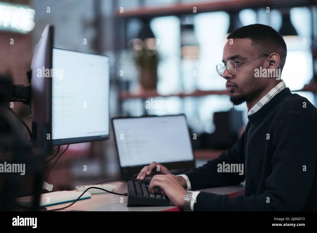 Giovane afroamericano con vetri seduti in un moderno ufficio di coworking e di lavoro ad un computer Foto Stock