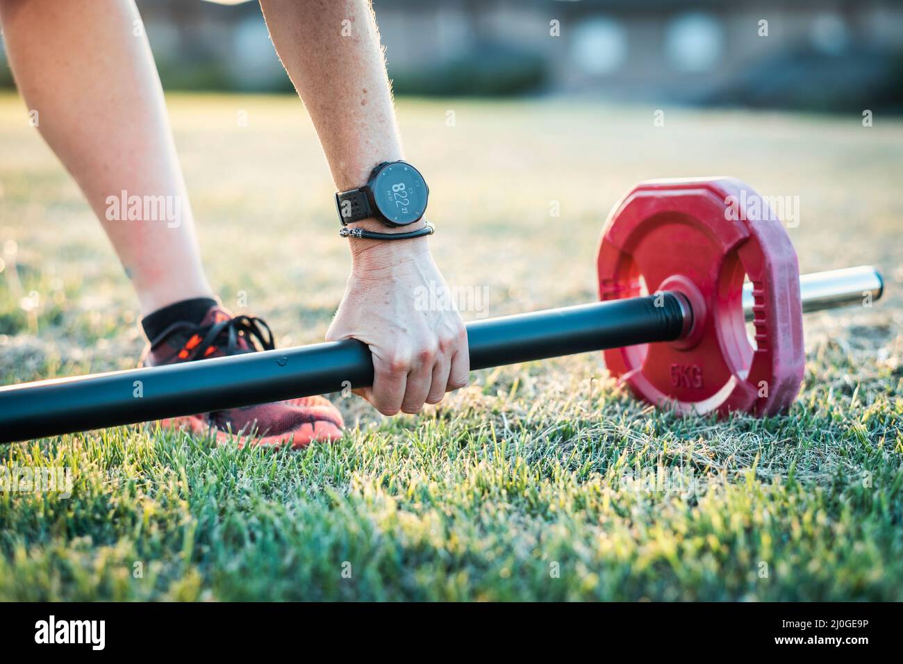 Donna matura in un parco con una barra di sollevamento pesi in un pomeriggio di sole. Concetto di fitness. Foto Stock