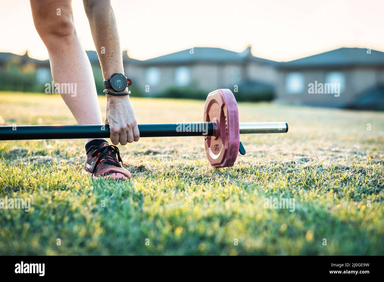 Donna matura in un parco con una barra di sollevamento pesi in un pomeriggio di sole. Concetto di fitness. Foto Stock