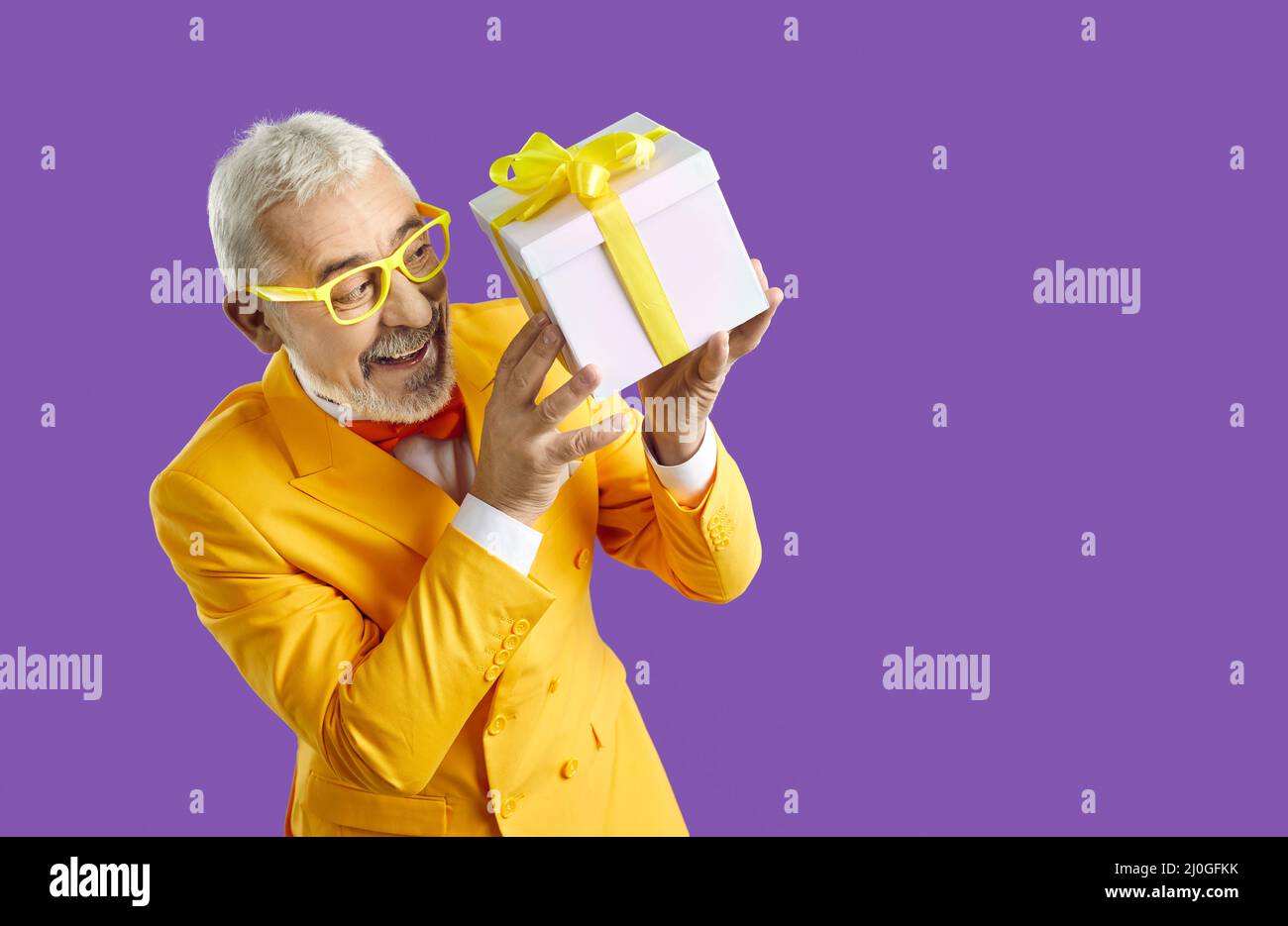 Felice uomo anziano divertente in un vestito giallo che tiene una scatola presente da una vendita di festa Foto Stock