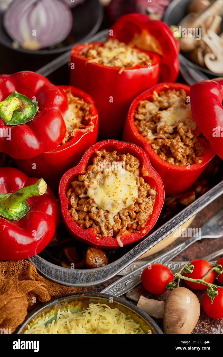 Peperoni di paprika ripieni di campana rossa in pentola da cucina con ferro da stiro vari ingredienti sul lato Foto Stock