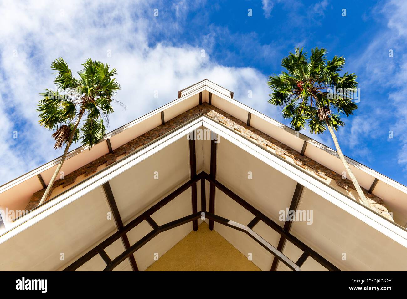 Tetto a chiesetta in stile coloniale, vista simmetrica ad angolo basso con due palme da cocco sui lati e cielo blu sullo sfondo Foto Stock