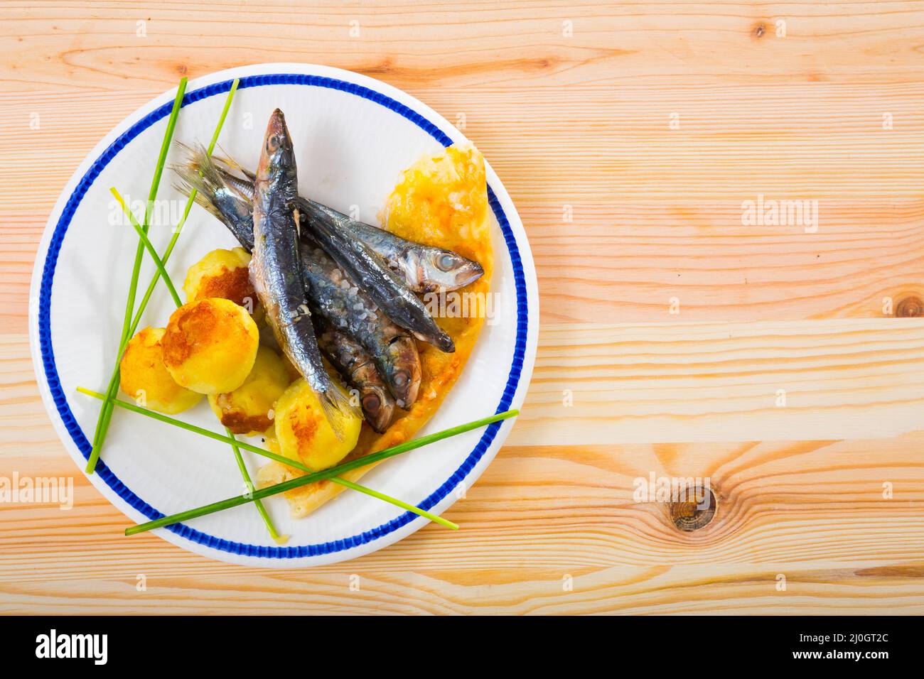 Vista dall'alto delle sardine fritte con patate su sfondo di legno Foto Stock