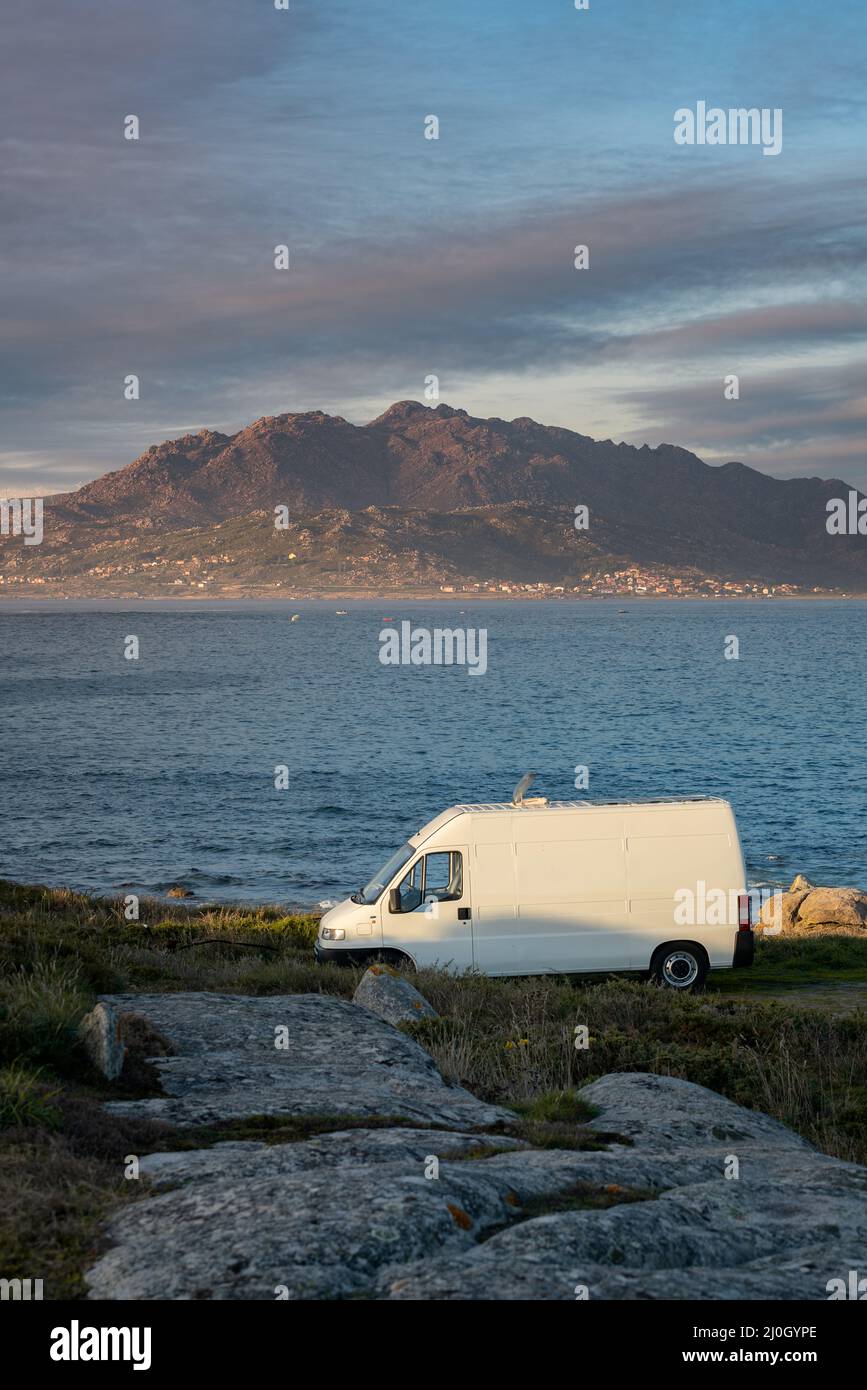Camper van motorhome con pannelli solari vista su un paesaggio marino con montagne che vivono van vita a Galiza, Spagna Foto Stock