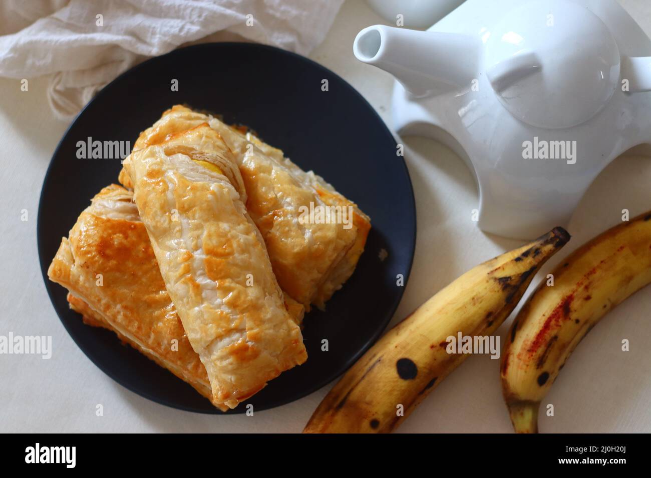 Spugnetta per plantain Fette di plantain mature avvolte in sfoglie e cotte fino a che croccanti. Girato su sfondo bianco insieme ad un mazzo di plantai maturi Foto Stock