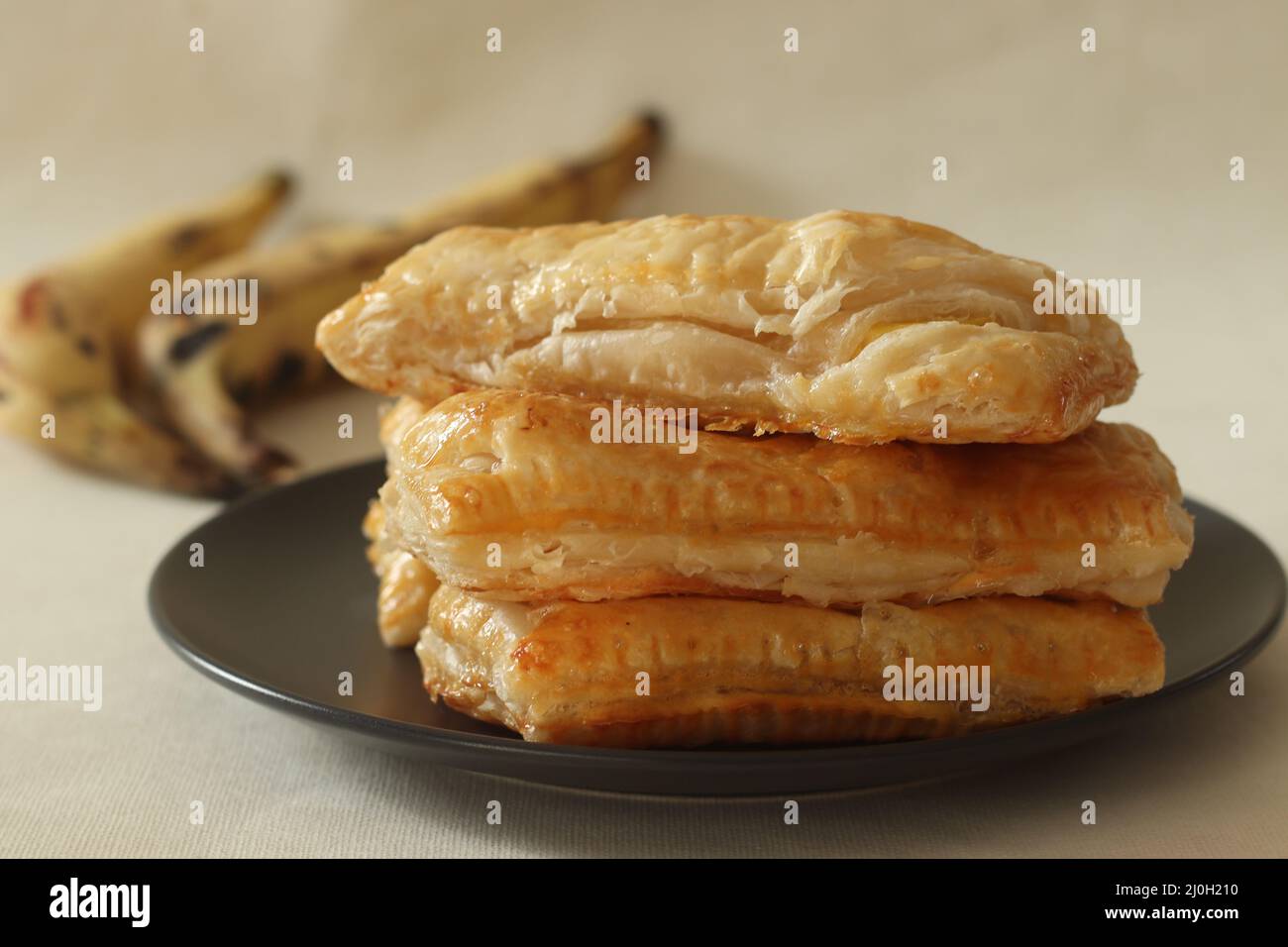 Spugnetta per plantain Fette di plantain mature avvolte in sfoglie e cotte fino a che croccanti. Girato su sfondo bianco insieme ad un mazzo di plantai maturi Foto Stock
