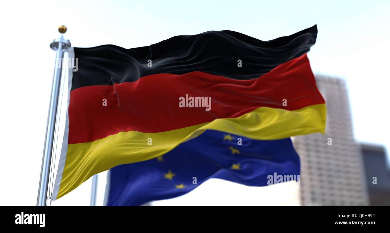 La bandiera nazionale della Germania che sventola nel vento insieme alla bandiera dell'Unione europea si è offuscata sullo sfondo Foto Stock