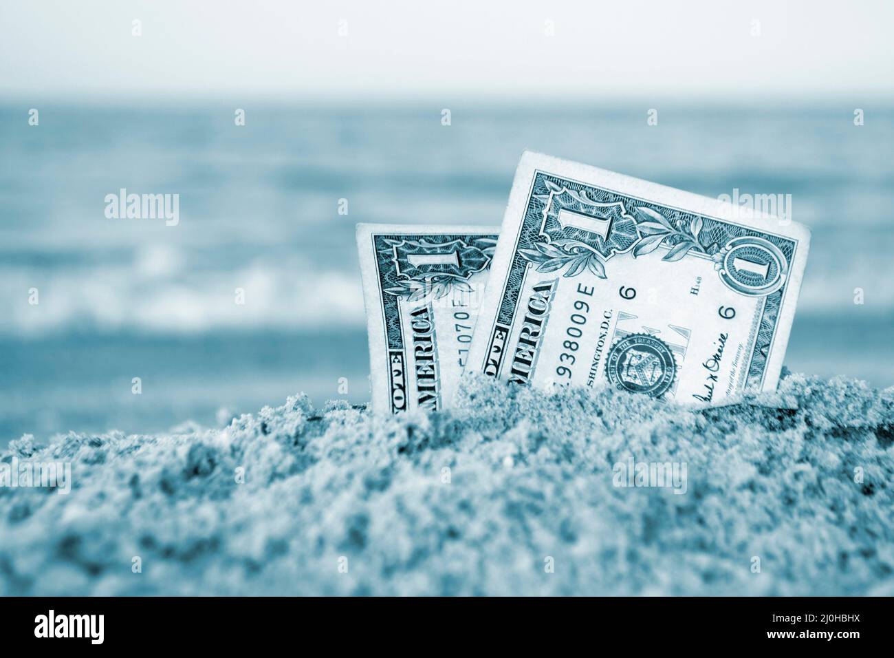 Due bollette da un dollaro mezzo sepolto in sabbia su sabbia sabbiosa spiaggia primo piano. Foto Stock
