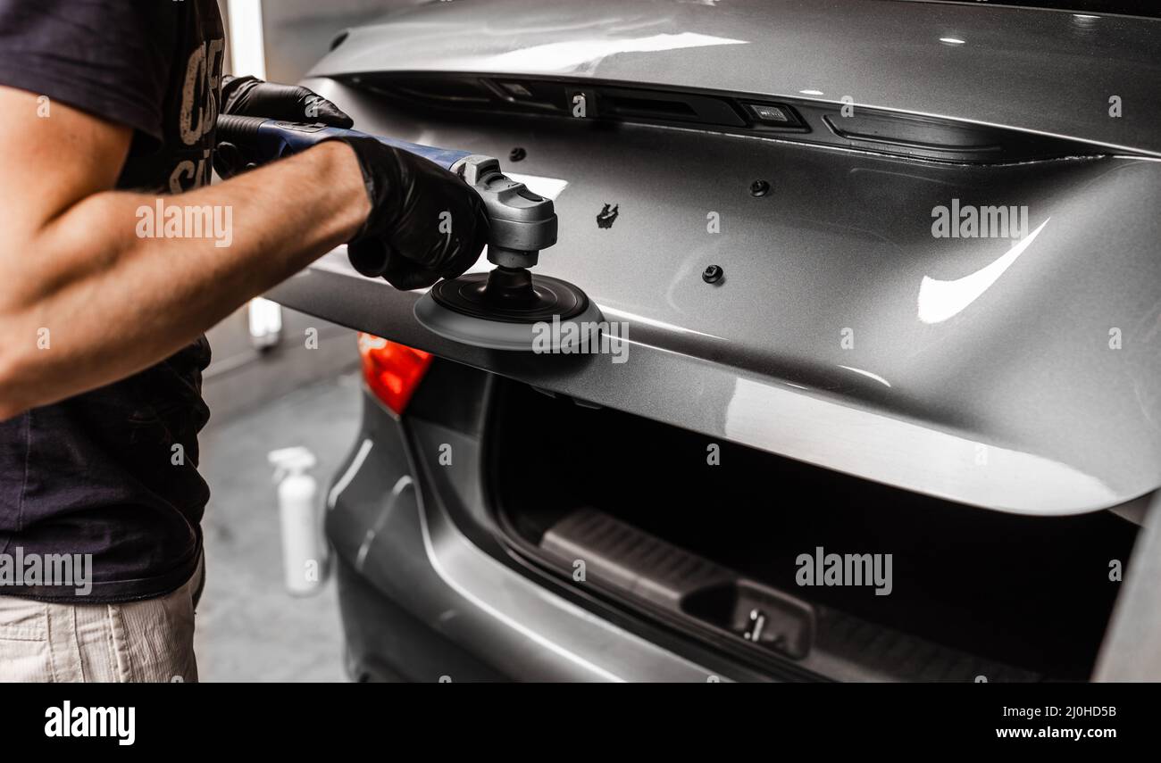 Dettaglio auto e concetto di lucidatura con il lavoratore maschile. Lucidare l'automobile grigia di lusso nel servizio auto. Foto Stock
