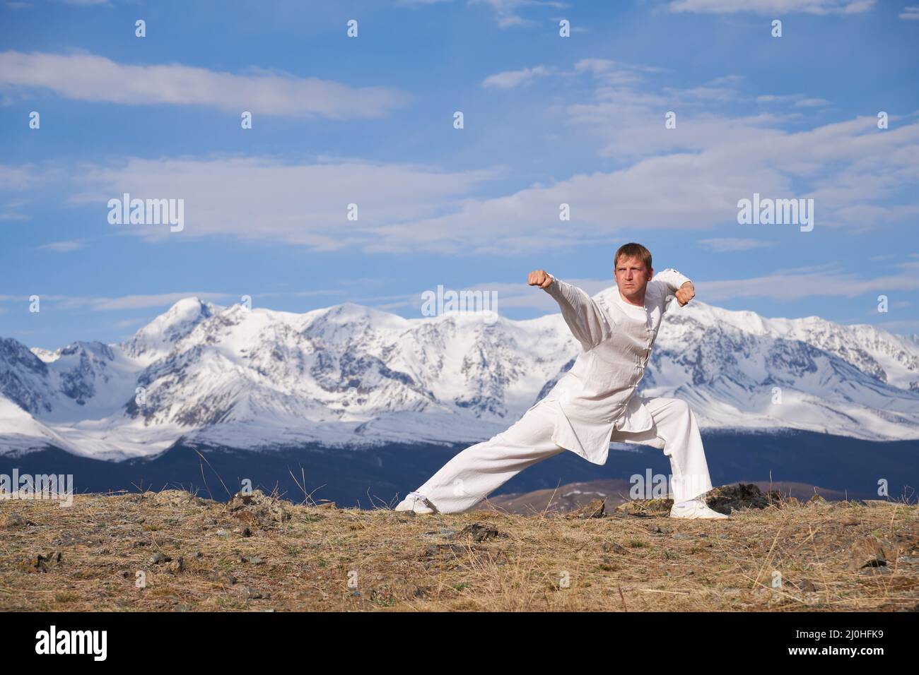 Wushu maestro in uno sport bianco uniforme di allenamento kungfu in natura sullo sfondo di montagne innevate. Foto Stock