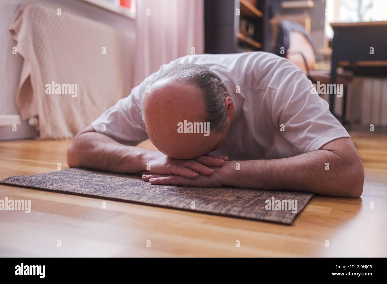 Uomo anziano meditando su un pavimento di legno e giacendo nella posa di Shavasana. Yoga attraente allenarsi a casa, fare yoga Foto Stock
