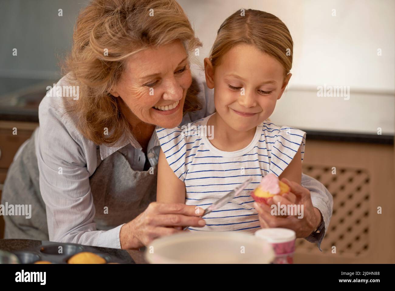 Condividere la sua saggezza cupcake. Shot di una bambina che decorano cupcakes con l'aiuto di sua nonna. Foto Stock