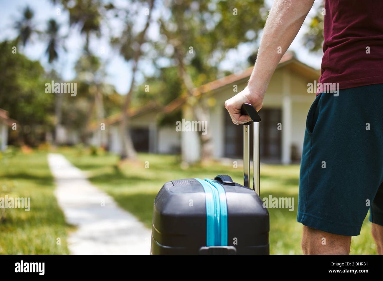 Uomo che tiene la valigia sul sentiero nel resort turistico di lusso. Ville d'hotel sotto le palme in una destinazione tropicale di viaggio. Foto Stock