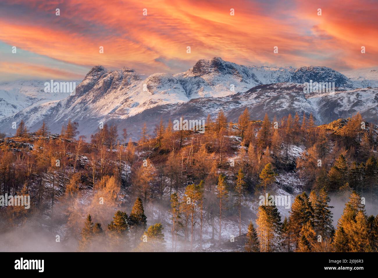 Un incredibile tramonto rosso e arancione sulle montagne innevate in una serata invernale nel Lake District inglese. Suggestivo paesaggio della Gran Bretagna. Foto Stock