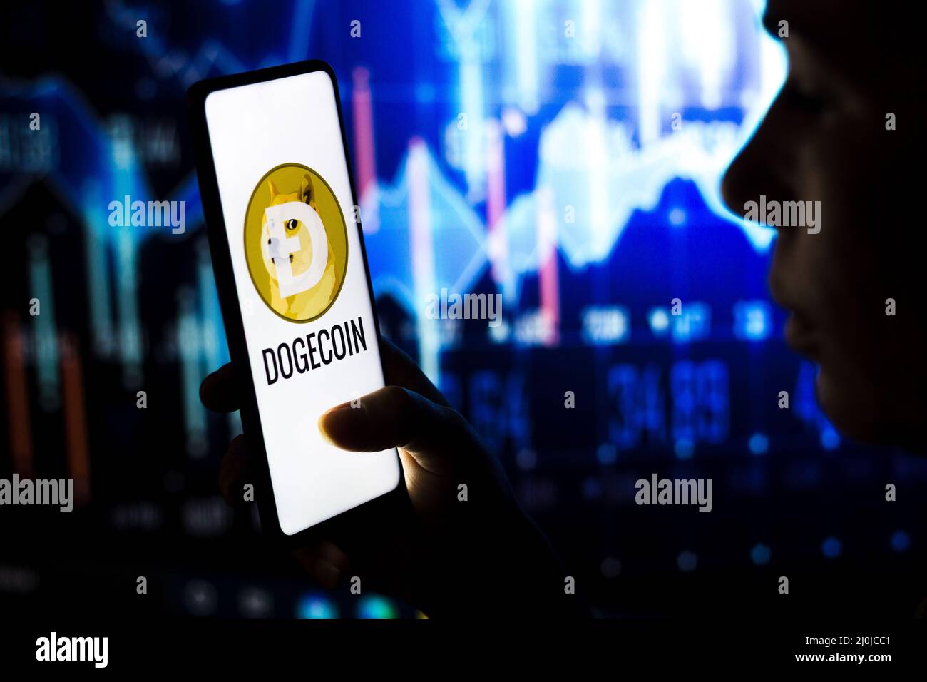 In questa foto, una donna tiene uno smartphone con il logo Dogecoin (DOGE) visualizzato sullo schermo. Foto Stock